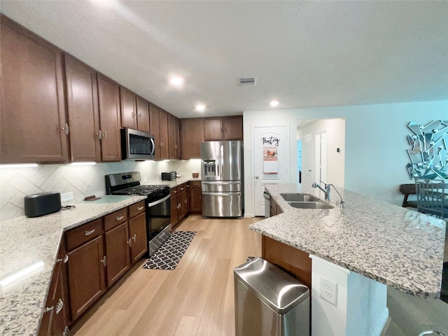 kitchen featuring sink, light stone countertops, stainless steel appliances, and light hardwood / wood-style flooring