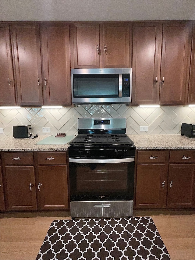 kitchen with light stone countertops, backsplash, appliances with stainless steel finishes, and light hardwood / wood-style flooring