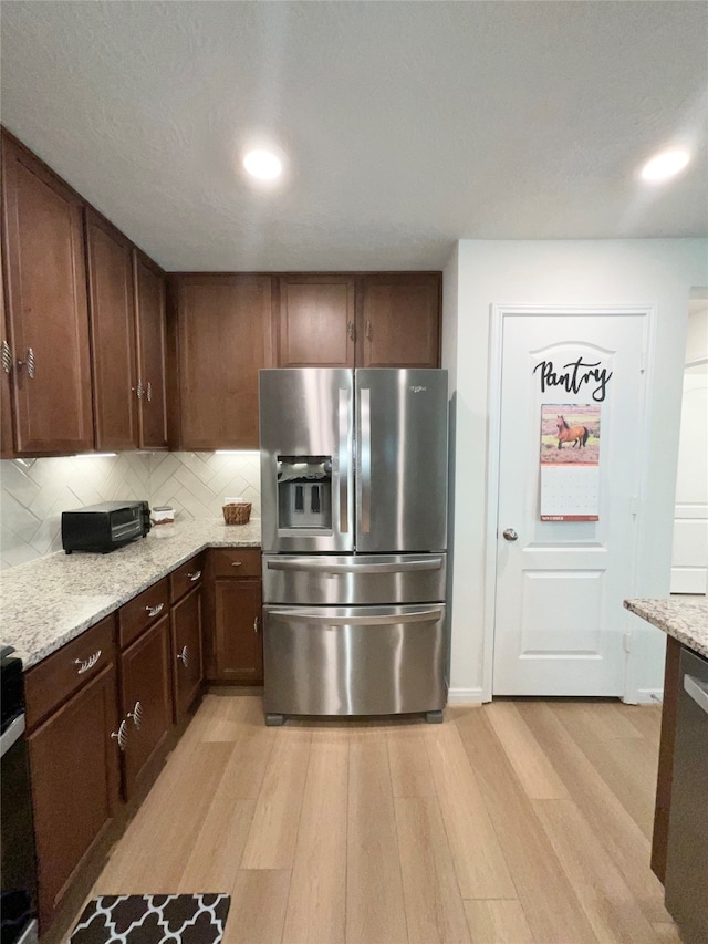 kitchen featuring light stone countertops, light hardwood / wood-style flooring, stainless steel refrigerator with ice dispenser, backsplash, and dark brown cabinets