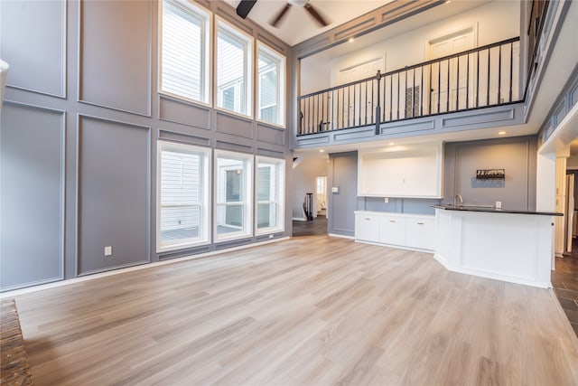 unfurnished living room with ceiling fan, a high ceiling, and light hardwood / wood-style flooring