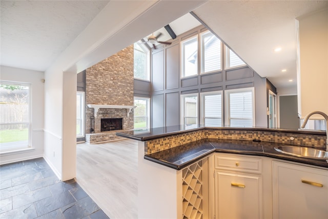 kitchen with kitchen peninsula, a textured ceiling, ceiling fan, sink, and a stone fireplace