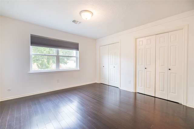 unfurnished bedroom with a textured ceiling, dark hardwood / wood-style floors, and multiple closets