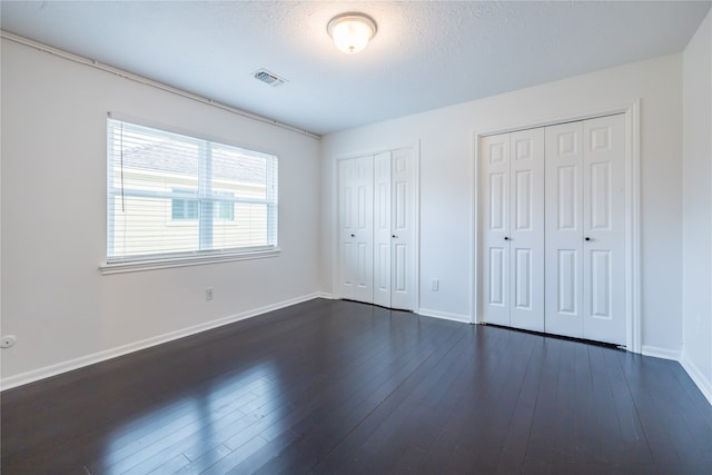 unfurnished bedroom with dark hardwood / wood-style flooring, a textured ceiling, and multiple closets