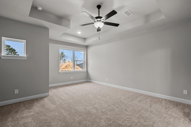 carpeted spare room with ceiling fan and a tray ceiling