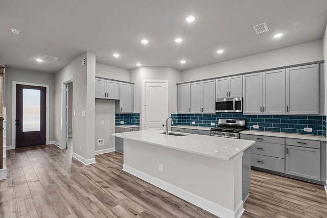 kitchen featuring stainless steel appliances, an island with sink, sink, and gray cabinets