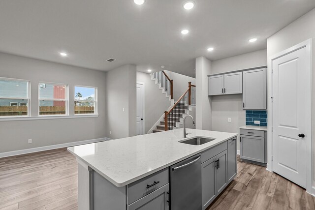 kitchen with sink, light stone counters, stainless steel dishwasher, a kitchen island with sink, and light hardwood / wood-style floors