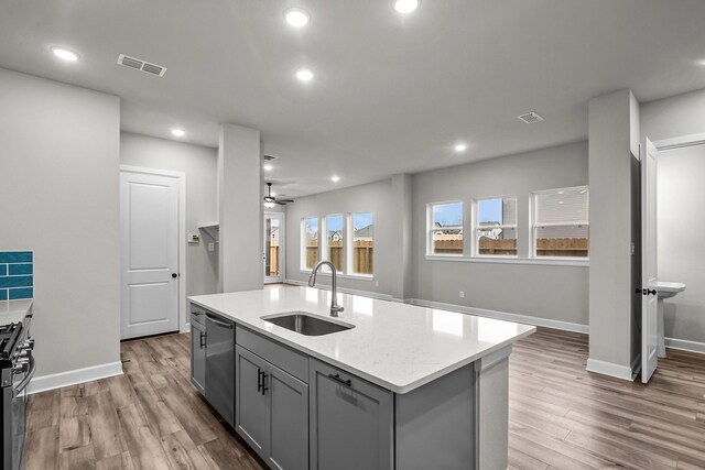 kitchen with sink, gray cabinets, appliances with stainless steel finishes, light hardwood / wood-style floors, and an island with sink