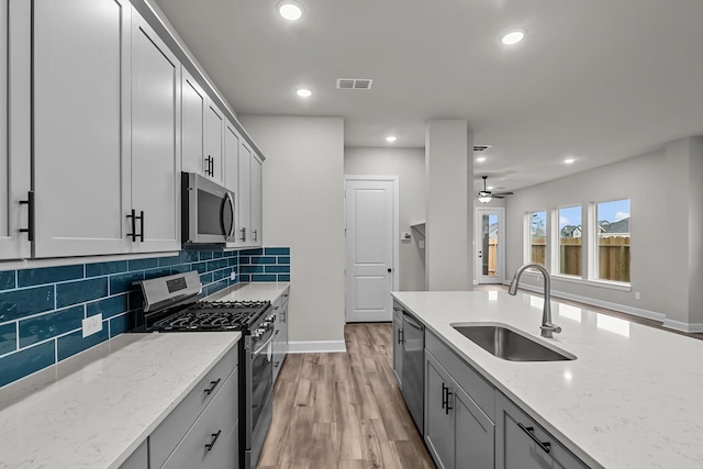 kitchen featuring appliances with stainless steel finishes, sink, decorative backsplash, light stone counters, and light hardwood / wood-style flooring