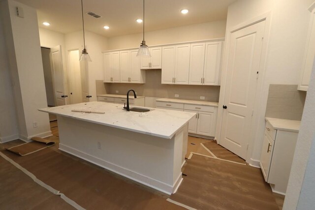 kitchen featuring light stone counters, decorative light fixtures, sink, and a center island with sink