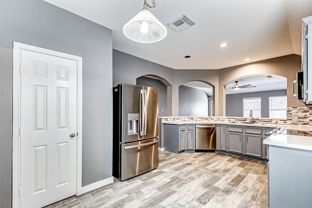 kitchen featuring stainless steel appliances, light hardwood / wood-style floors, decorative light fixtures, gray cabinets, and decorative backsplash