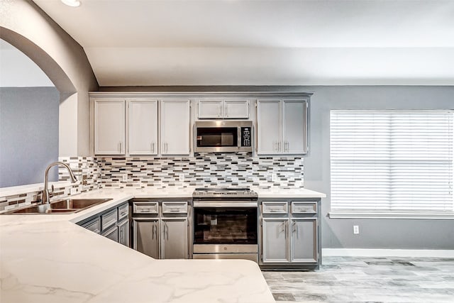 kitchen with light wood-type flooring, backsplash, gray cabinetry, stainless steel appliances, and sink