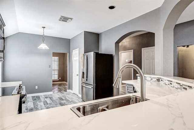 kitchen with light stone countertops, sink, pendant lighting, lofted ceiling, and appliances with stainless steel finishes