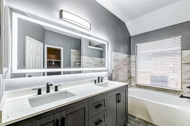 bathroom featuring wood-type flooring, vanity, vaulted ceiling, and a bathing tub