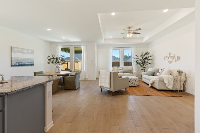 living room with ceiling fan, a healthy amount of sunlight, a tray ceiling, and light hardwood / wood-style flooring