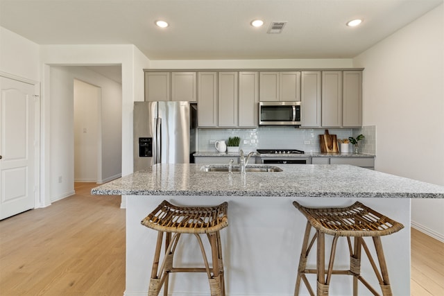 kitchen with light stone countertops, appliances with stainless steel finishes, light hardwood / wood-style floors, sink, and gray cabinets