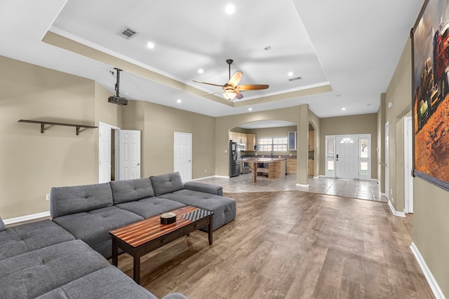 living room with light hardwood / wood-style floors, a raised ceiling, and ceiling fan