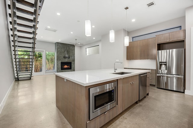 kitchen featuring pendant lighting, a center island with sink, sink, a fireplace, and appliances with stainless steel finishes