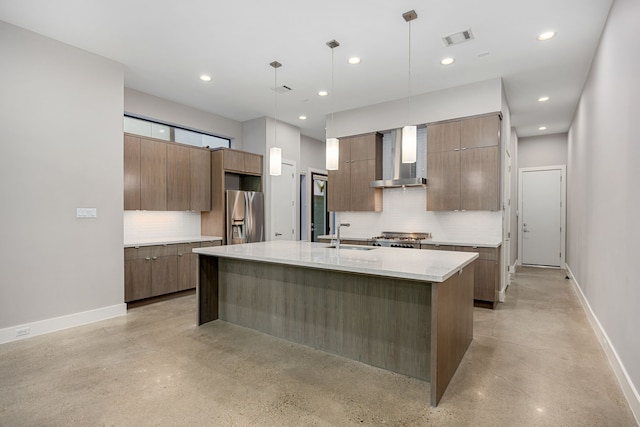 kitchen with appliances with stainless steel finishes, backsplash, wall chimney exhaust hood, hanging light fixtures, and an island with sink