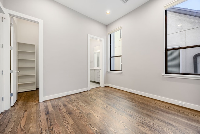 unfurnished bedroom with ensuite bathroom, dark hardwood / wood-style floors, a spacious closet, and a closet