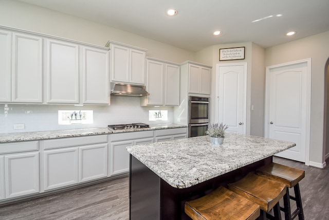 kitchen with white cabinets, appliances with stainless steel finishes, a center island, and hardwood / wood-style flooring