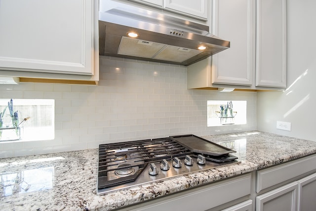 kitchen with light stone countertops, backsplash, extractor fan, stainless steel gas cooktop, and white cabinetry