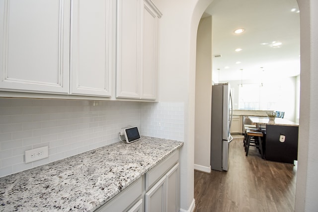 kitchen featuring light stone countertops, dark hardwood / wood-style floors, stainless steel refrigerator, and white cabinetry