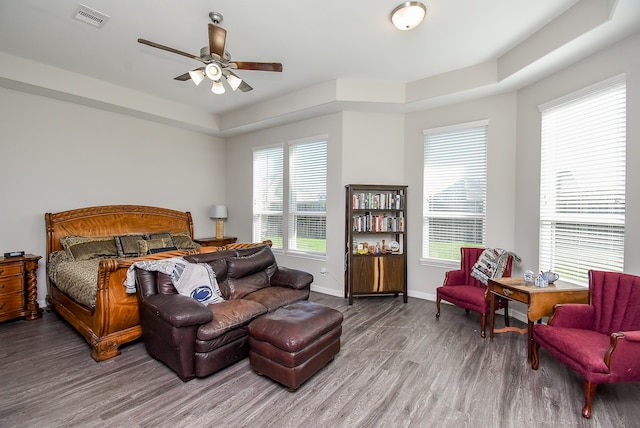 bedroom featuring hardwood / wood-style flooring, a raised ceiling, multiple windows, and ceiling fan