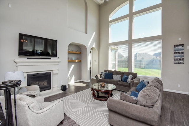 living room with built in shelves, a wealth of natural light, a towering ceiling, and dark hardwood / wood-style floors