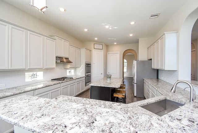 kitchen with a center island, sink, dark wood-type flooring, stainless steel appliances, and light stone counters