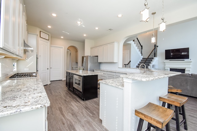 kitchen featuring white cabinetry, backsplash, pendant lighting, a center island with sink, and appliances with stainless steel finishes