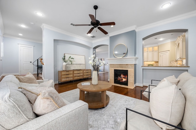 living room with dark hardwood / wood-style flooring, ceiling fan, crown molding, and a tiled fireplace