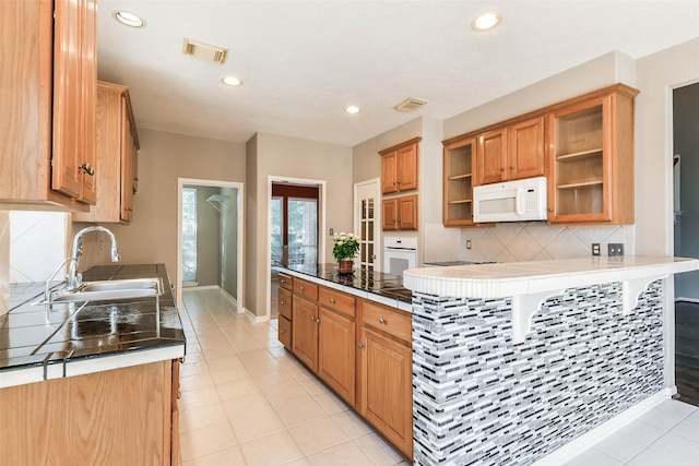 kitchen with kitchen peninsula, white appliances, sink, tile countertops, and light tile patterned flooring