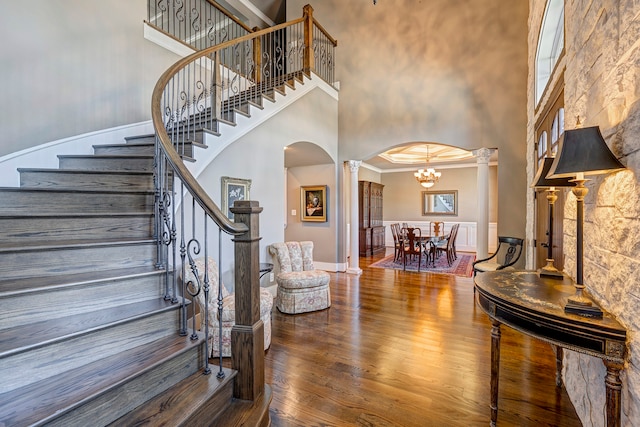 entryway with decorative columns, a high ceiling, ornamental molding, wood-type flooring, and a chandelier