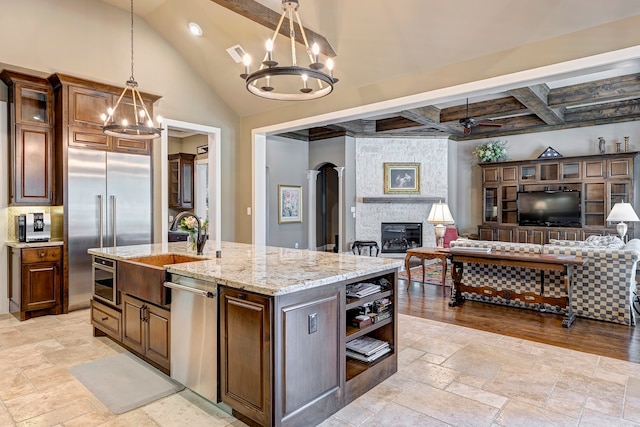 kitchen with ceiling fan with notable chandelier, stainless steel appliances, hanging light fixtures, a fireplace, and a center island with sink