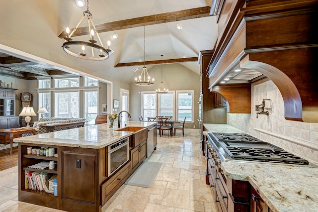 kitchen with a kitchen island with sink, sink, hanging light fixtures, light stone countertops, and tasteful backsplash