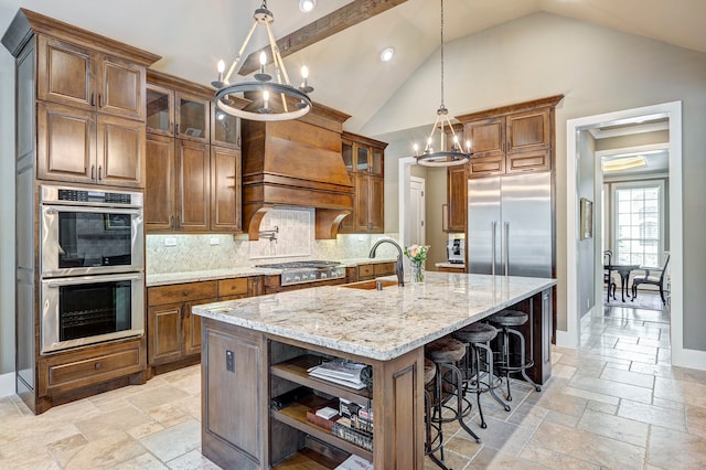 kitchen with backsplash, stainless steel appliances, a kitchen island with sink, sink, and hanging light fixtures