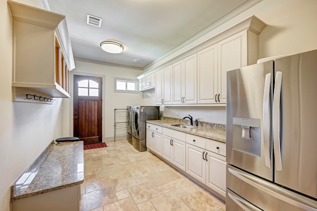 kitchen with light stone countertops, stainless steel fridge with ice dispenser, washer and clothes dryer, and sink