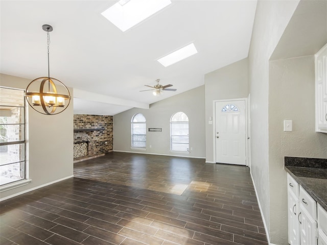 unfurnished living room with a brick fireplace, ceiling fan with notable chandelier, dark hardwood / wood-style floors, and lofted ceiling with skylight