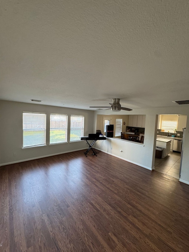 unfurnished living room with ceiling fan, dark hardwood / wood-style flooring, and a textured ceiling