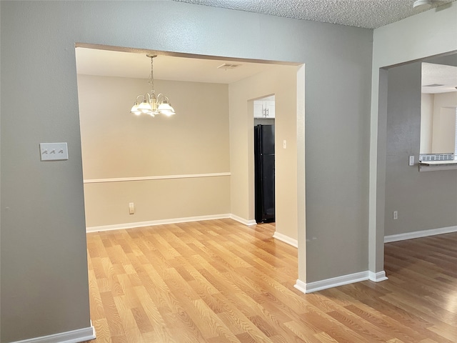 unfurnished room with light hardwood / wood-style floors, a textured ceiling, and a notable chandelier