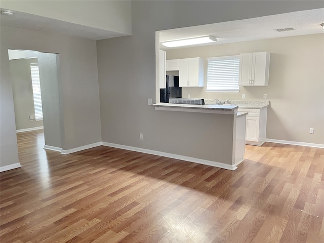 kitchen with white cabinets, a textured ceiling, light hardwood / wood-style floors, and black refrigerator