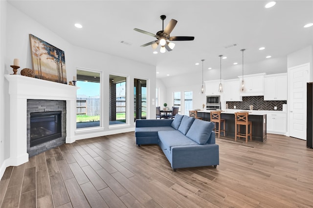 living room featuring ceiling fan, a stone fireplace, and wood-type flooring