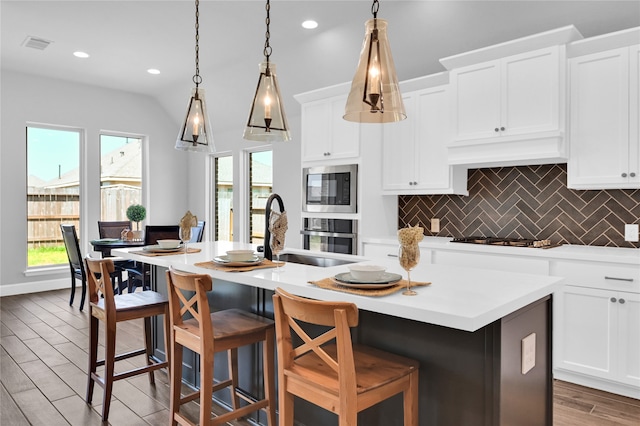 kitchen featuring decorative light fixtures, a breakfast bar area, a center island with sink, appliances with stainless steel finishes, and hardwood / wood-style flooring