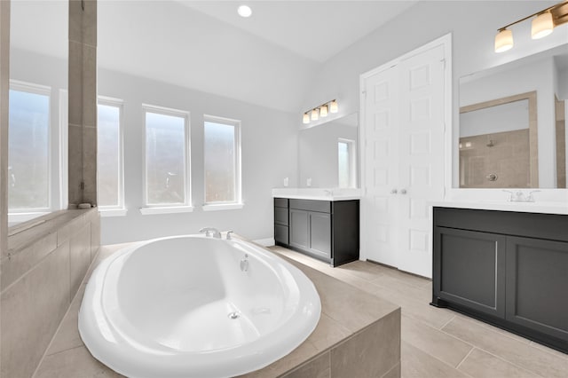 bathroom with tiled tub, tile patterned flooring, vanity, and vaulted ceiling