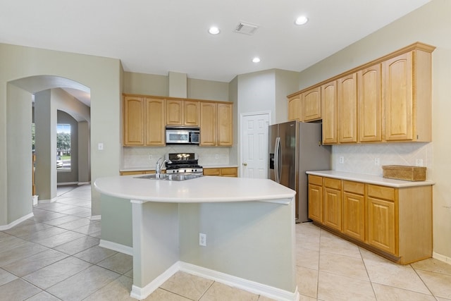 kitchen featuring appliances with stainless steel finishes, backsplash, sink, light tile patterned floors, and an island with sink