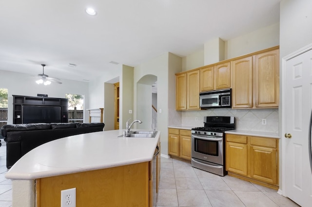 kitchen with a kitchen island with sink, sink, decorative backsplash, ceiling fan, and stainless steel appliances