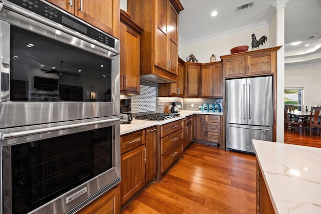 kitchen with light stone countertops, appliances with stainless steel finishes, decorative backsplash, crown molding, and hardwood / wood-style flooring