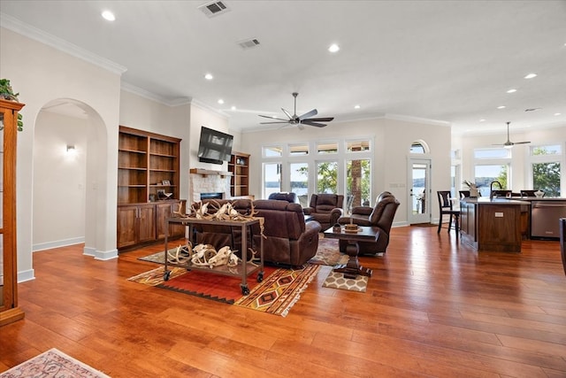 living room with a stone fireplace, crown molding, plenty of natural light, and wood-type flooring