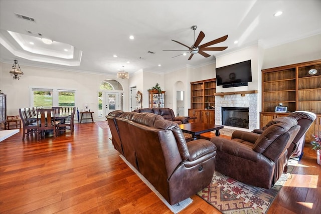 living room with a stone fireplace, crown molding, wood-type flooring, and ceiling fan with notable chandelier