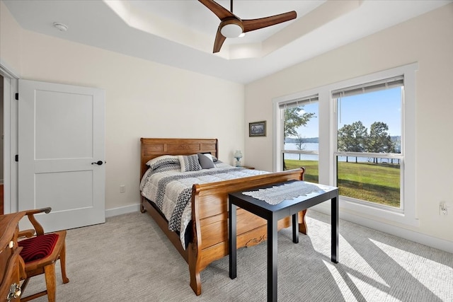 bedroom with ceiling fan, light colored carpet, a water view, and a tray ceiling